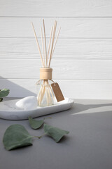 Fototapeta na wymiar Aroma diffuser in a clear glass bottle with a wooden cap on a light wooden-concrete background and green eucalyptus leaves. Front view