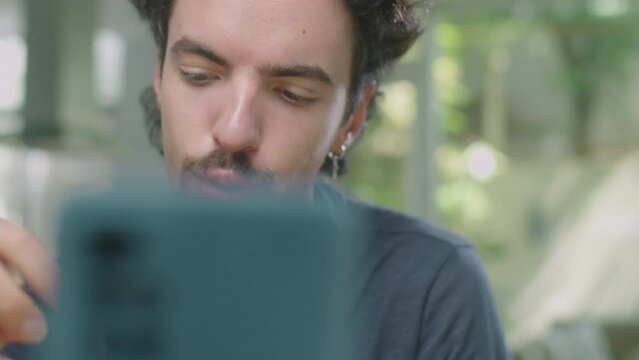 Close up shot of male beauty vlogger applying fixing gel to eyebrows and talking on smartphone camera while filming makeup tutorial or streaming at home