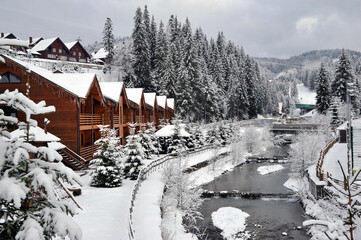 Christmas winter landscape. Wooden cottages holiday houses in mountain holiday resort on the shore of a mountain river.