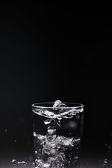 natural mineral clean healthy water in a transparent glass and drops of water splash out of it on a dark background. for banners labels splash screens postcards advertising signage