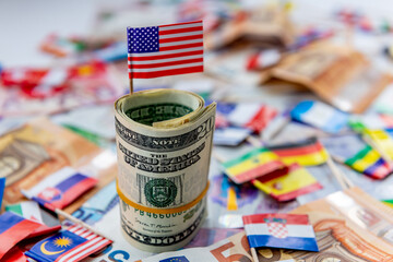 A roll of US dollars with the American flag on top of a other currencies and country flags. Dollar hegemony concept. - obrazy, fototapety, plakaty