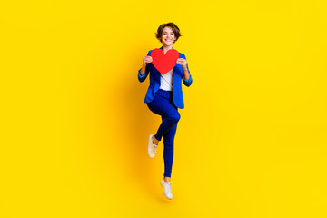 Fototapeta na wymiar Full length photo of sweet shiny woman wear blue jacket rising big red heart jumping high isolated yellow color background