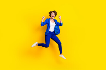 Fototapeta na wymiar Full length photo of shiny lucky woman wear blue jacket rising fists screaming jumping high isolated yellow color background