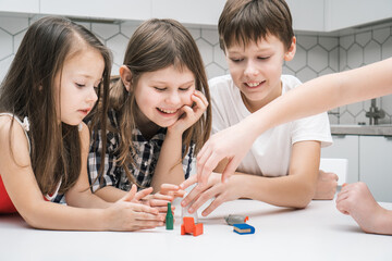 Happy little school kids play toy mini furniture on kitchen table. Portrait of group of friends...