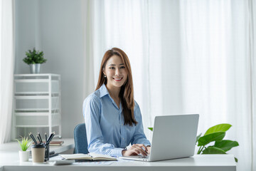 Beautiful Asian businesswoman sitting at work saving data Happy checking financial details on laptop computer in the office.