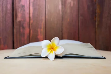 Zelfklevend Fotobehang Plumeria flower on open book with space on wood background, flower book, education concept © sirirak