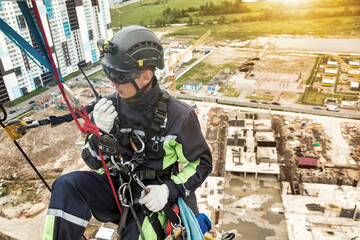 Industrial mountaineering worker in uniform talking walkie-talkie hangs on wall skyscraper at...