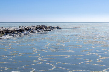 Close-up of the icy seashore, frozen waves, rocks and sun glare on the ice