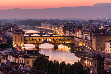 The illuminated Ponte Vecchio over Arno river in an orange and purple twilight.