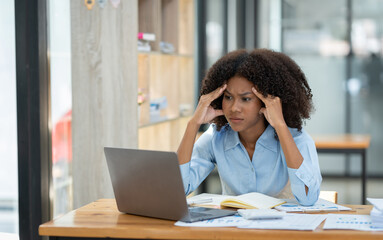 Young American businesswoman working on the laptop with documents and stressing at work from working on financial documents in office Overworked woman concept.