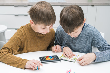 Happy schoolboys play toy constructor sitting at table. Children collect colored details on playing plastic board. Kids read game rules, instruction. Educational interesting board game.