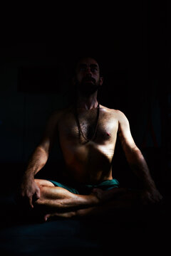 silhouette portrait isolated on dark background of mid adult male yogi sitting in lotus position meditating