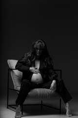 Beautiful pregnant girl at the studio. A pregnant girl in a man's suit.Stunning pregnant woman - maternity photography of a beautiful young expecting mother to be on a black background, studio photogr