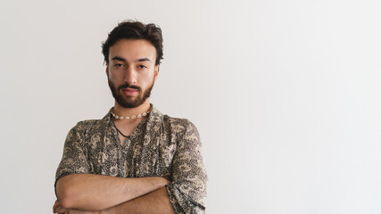 Obraz premium Panoramic photo of a young queer gay latin man looking at camera with his arms crossed on a white background. Copy space.