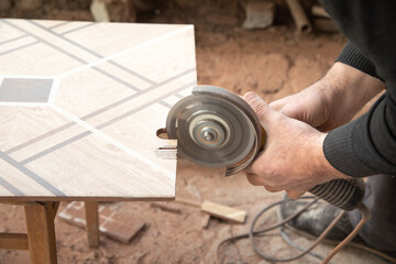 Worker cutting a ceramic tile with a grinder.