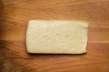 Slice of Casera cheese on a wooden cutting board. Typical cheese from Valtellina, Italy