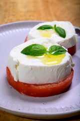 Sliced white ball of Italian soft cheese Mozzarella di Bufala Campana served with fresh green basil and red tomato