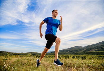 man runner running summer mountain meadow in background blue sky