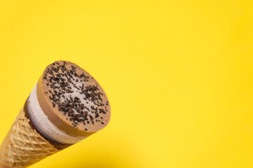 Delicious chocolate ice cream cone, summer dessert on yellow background. Cool minimal flat lay, copy space