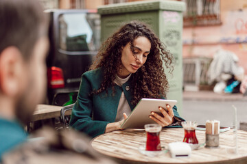 Fototapeta premium Beautiful curly businesswoman using digital tablet outdoors in cafe
