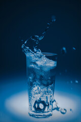 natural mineral healthy water in a transparent glass and drops of water splash out of the glass on a blue background. for signage banners labels postcards advertising