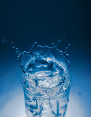 natural mineral healthy water in a transparent glass and drops of water splash out of the glass on a blue background. for signage banners labels postcards advertising