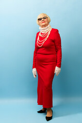 Fashionable look. Beautiful old woman, grandmother in stylish red dress and pearl necklace posing...