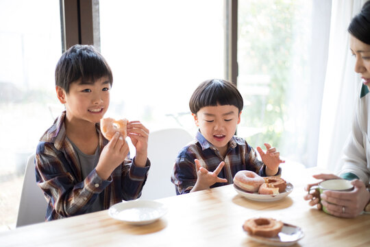 おやつのドーナツを食べる兄弟とそれを見守る母親