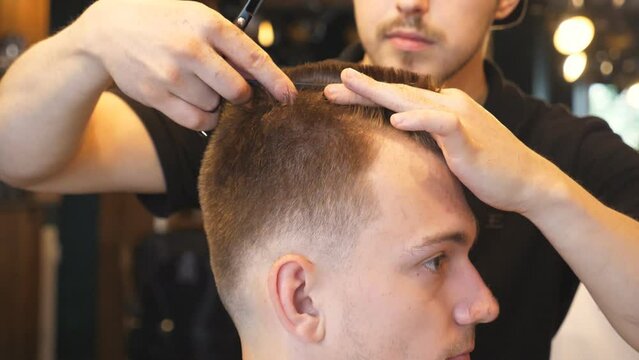 Male hand of professional hairstylist combing hair of his customer in salon. Young guy getting his hair dressed at trendy barbershop. Hairstyling process. Close up Side view Slow motion