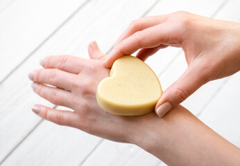 Woman hands holding and applying handmade beeswax and shea butter solid moisturizing hand cream....