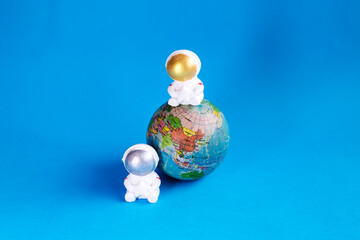 Two decorative astronauts sitting on earth on blue background 