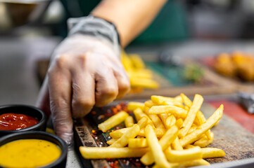 chef in cooking gloves serving french fries on wooden board.