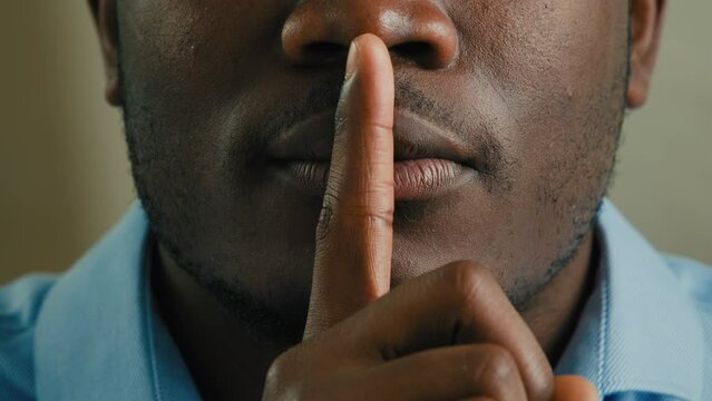 Close up part face man silent mysterious african american 30s male businessman put finger to lips make silence hush gesture mystery not saying keep secret stop talk privacy information tell secrecy