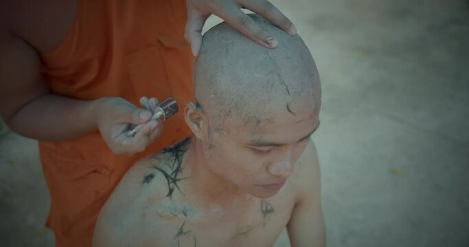 A slow-motion scene of a man who must be over twenty years old having his hair shaved to become a Buddhist monk which is Theravada sect in Thailand.