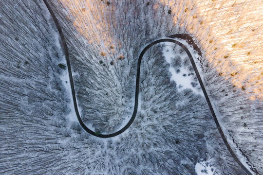 Aerial view of vehicle driving a serpentine forest road in wintertime with snow on Mount Terminio, Serino, Avellino, Irpinia, Campania, Italy.