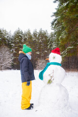 Fototapeta na wymiar happy child stands next to snowmen in winter in a snowy forest