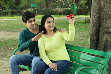Young Indian Happy couple sitting on a park bench in a serene atmosphere playing with a paper...