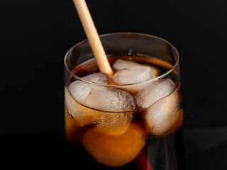 Glass of cola with ice on a black background. Close-up.