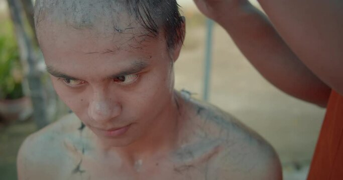A slow-motion scene of a man who must be over twenty years old having his hair shaved to become a Buddhist monk which is Theravada sect in Thailand.