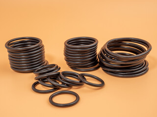 Hydraulic and pneumatic o-rings in black in different sizes on an orange background. Rubber gaskets for plumbing. copy space.