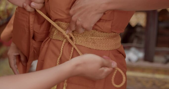 A slow-motion scene of a man who must be over twenty years of age changing into a robe to become a Buddhist monk which is Theravada sect in Thailand.