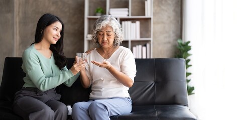 Asian daughter giving pills to mother helping her mom taking medicine with glass of water