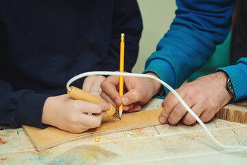 Obraz premium Boy burn out numbers with soldering iron on wooden disc. Kid makes wooden clock in the workshop.
