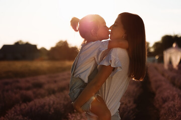 family day. young mom and little daughter enjoy relaxing in a field with lavender at sunset. A beautiful mother hugs and kiss child girl tightly. Maternal care and love for the child. mothers day