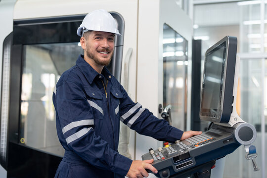 Male engineer operating cnc machine in control panel at factory. Smiling man technician in uniform and helmet safety working at workshop heavy metal industrial