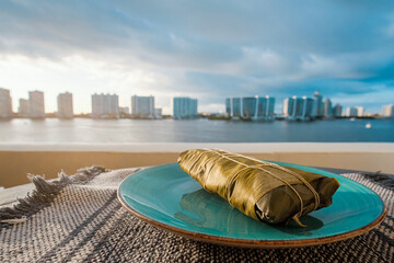 Hallaca or Tamale over a rustic table and a blue dish with a drink, Mexican and Venezuelan...