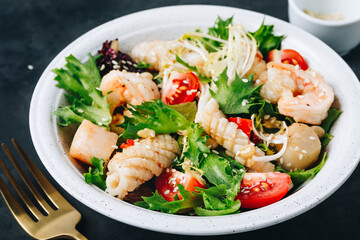 Seafood salad bowl. Green lettuce tomato salad with shrimps, scallop and squids