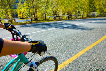 Fototapeta na wymiar Cyclist in protective gloves rides along the track along the yellow markings in sunny clear weather. Active lifestyle, cycling in the golden autumn in the mountains