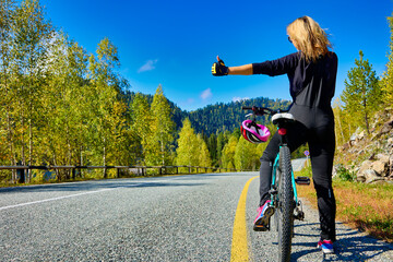 View from behind slender young woman in black suit on bicycle, standing on side road, voting with...