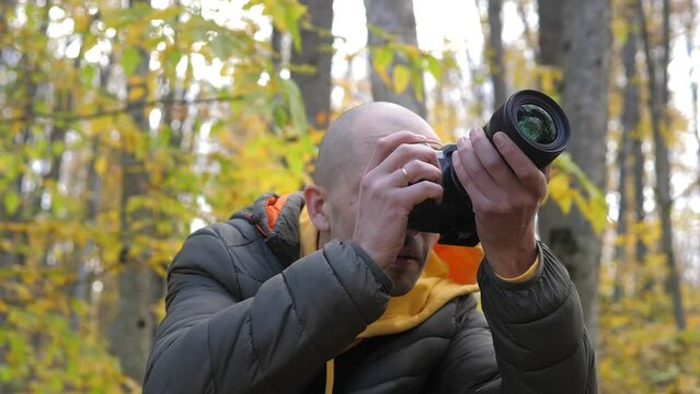 Portrait of the interested photographer looking up at the autumn forest landscape, leaning into his camera, pressing shutter release and taking some photos. Active tourism and hobby concept. 